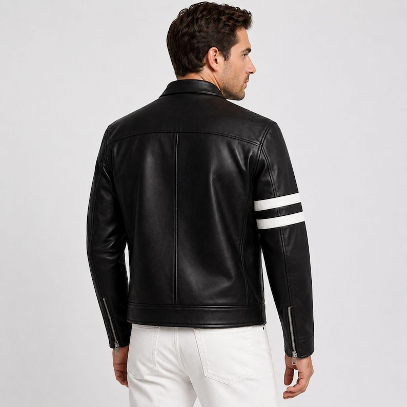 May include: Black leather jacket with white stripes on the sleeves. The jacket features a classic collar, zip details on the sleeves, and a tailored fit. The model is wearing white trousers.
