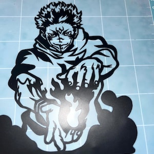 Puede incluir: Calcomanía de vinilo negro de un personaje con pelo puntiagudo, una sudadera con capucha y una expresión decidida. Las manos del personaje están extendidas, con un efecto de energía ardiente. Sobre una superficie azul claro.