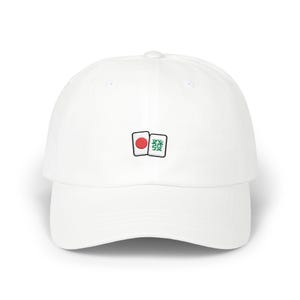 May include: White baseball cap with a curved brim. The cap features an embroidered design of two Mahjong tiles: one with a red dot and the other with a green character. The cap is a classic, casual accessory.