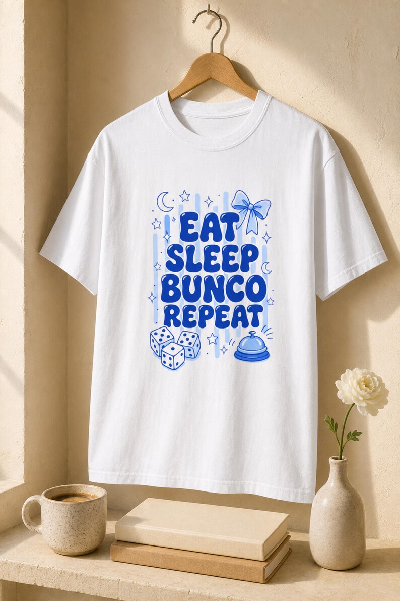 'Eat Sleep Bunco Repeat' bunco dice graphic tee on a wood hanger in a warm editorial wellness setting — bunco group tee lifestyle gift, chest print sharp and legible, styled hanger shot.