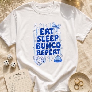 'Eat Sleep Bunco Repeat' printed graphic tee — bunco lifestyle gift shirt styled in a sunlit game-night flat lay with dice, scorecard, and latte. Comfort Colors garment-dyed t-shirt for bunco lovers.