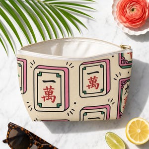 Mahjong tile-print accessory pouch — mahjong lover gift pouch — in a bright overhead flat lay on white marble with palm frond, ranunculus, and citrus props. Fully open showing tile print.