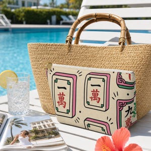 Mahjong tile-print accessory pouch on a white poolside lounge chair beside a straw tote — mahjong lover gift pouch in a bright resort lifestyle scene with turquoise pool background.