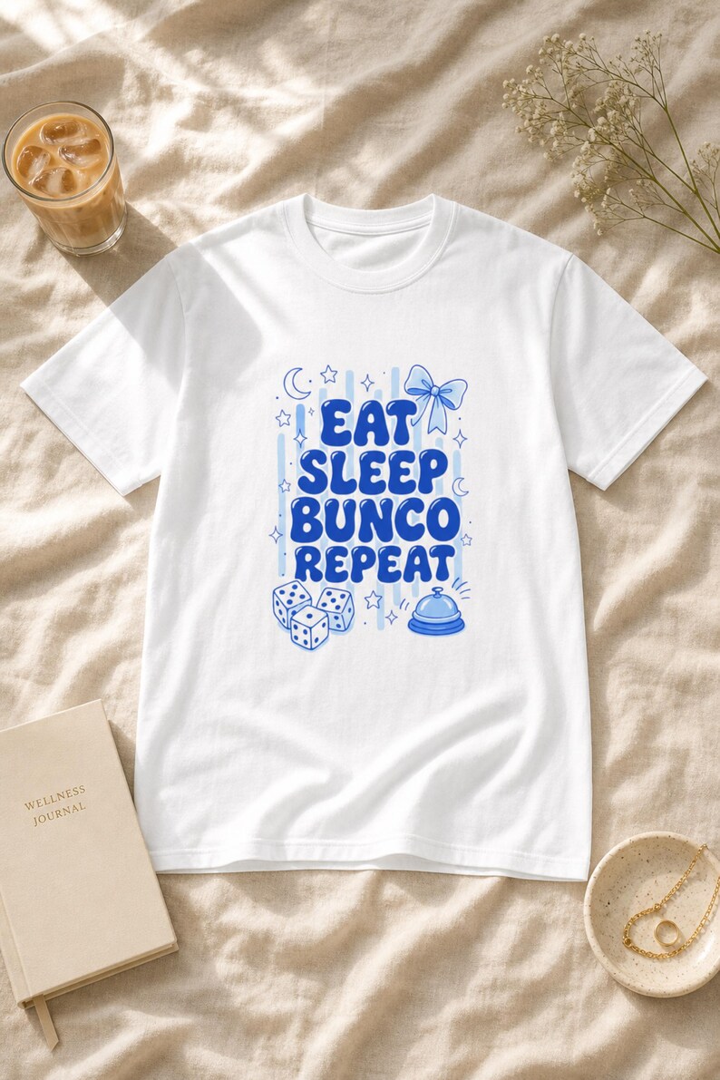 'Eat Sleep Bunco Repeat' printed t-shirt bunco dice graphic tee in a sunlit cream linen flat lay with wellness props — perfect bunco night gift or bunco group tee.