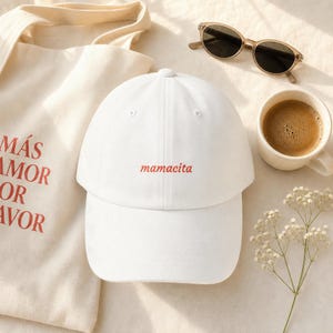 White “mamacita” embroidered dad hat styled flat lay with tote bag, coffee and sunglasses on neutral background