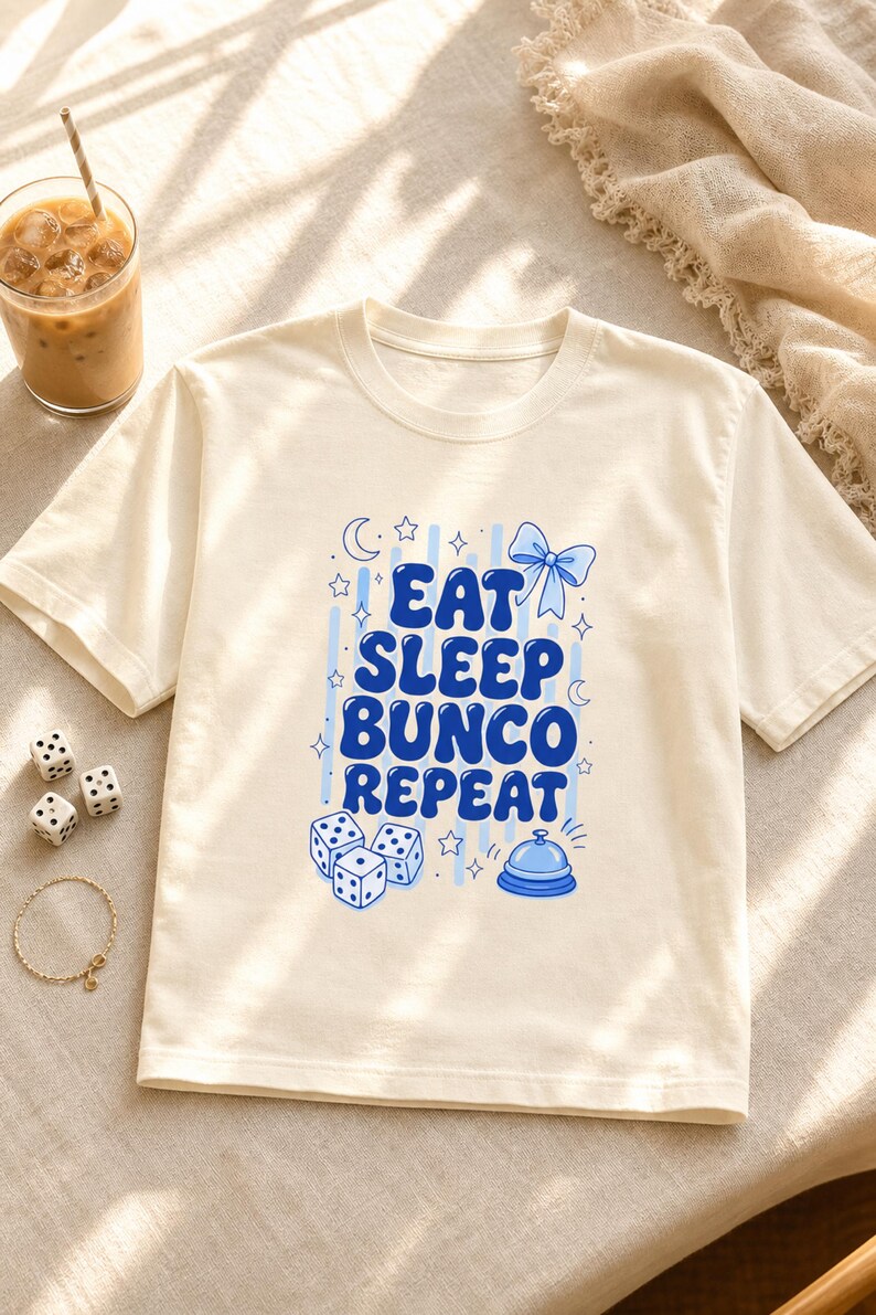 'Eat Sleep Bunco Repeat' bunco dice graphic tee styled in a warm bunco night table scene with dice and wellness props — bunco lifestyle gift shirt, chest print fully visible editorial flat lay.