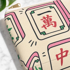 Close-up of mahjong tile-print accessory pouch showing tile pattern and zipper detail — mahjong print pouch gift, macro editorial shot on white marble.