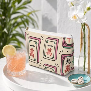 Mahjong tile-print accessory pouch — mahjong gift pouch — shown upright on a glossy white lacquer tray on a sunny patio, styled with a citrus spritz and orchid bud vase.