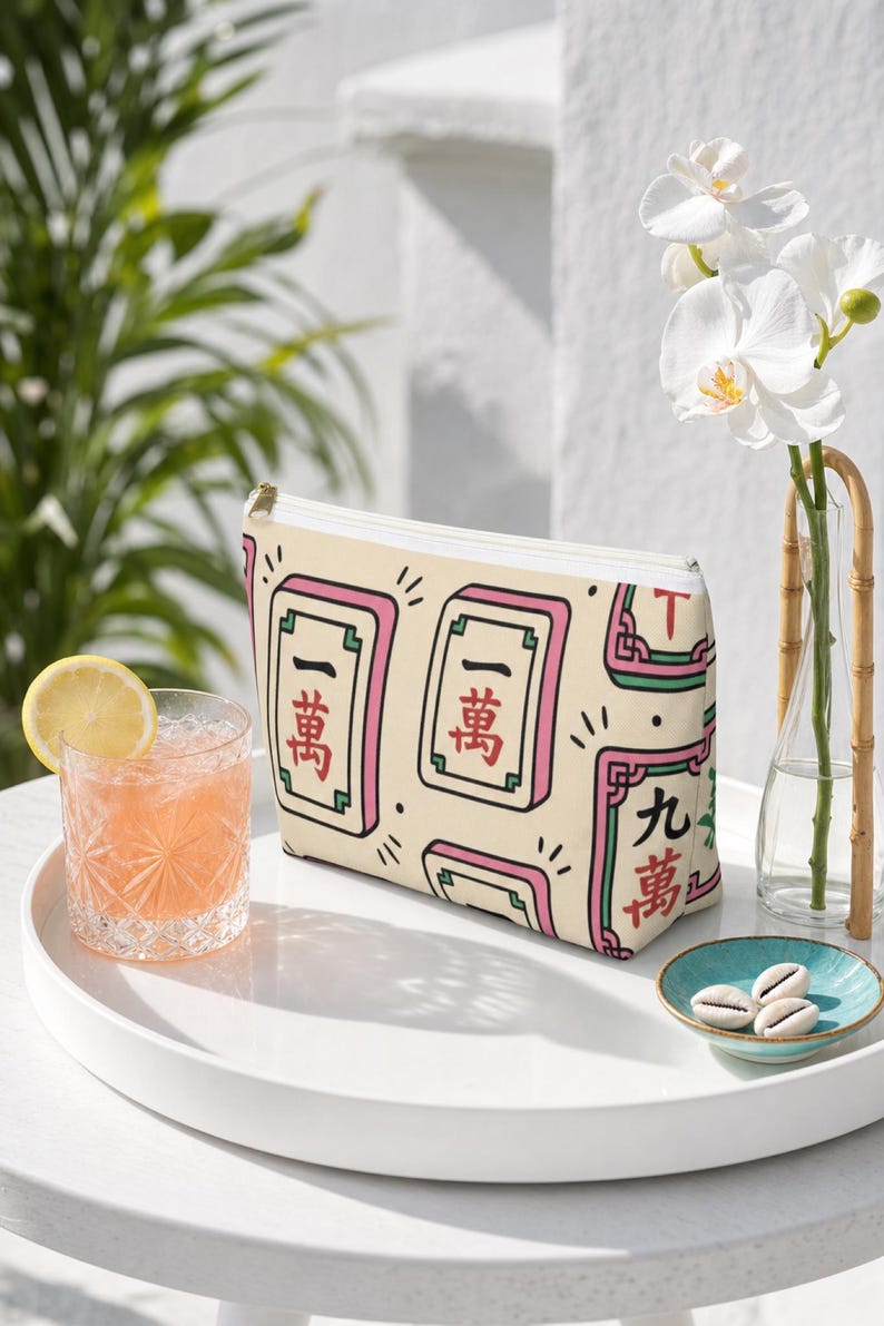 Mahjong tile-print accessory pouch — mahjong gift pouch — shown upright on a glossy white lacquer tray on a sunny patio, styled with a citrus spritz and orchid bud vase.