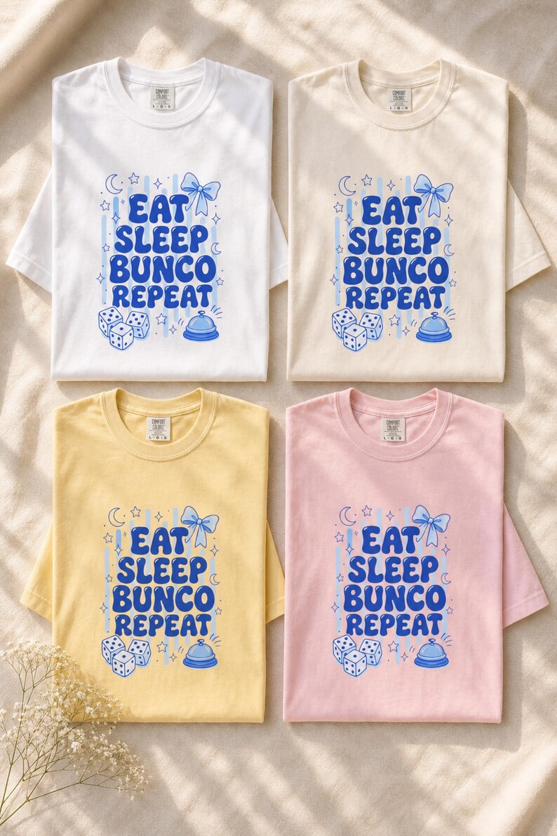 'Eat Sleep Bunco Repeat' bunco dice graphic tee in 4 garment-dyed colorways — bunco lifestyle gift tee color options overhead flat lay, all chest prints legible, editorial wellness scene.