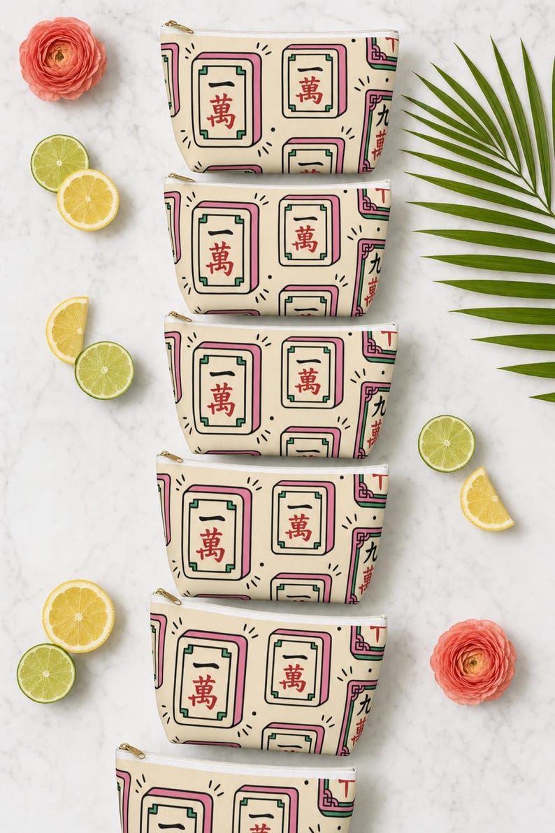 Multiple colorways of the mahjong tile-print accessory pouch in an overhead flat lay on white marble — mahjong gift pouch color options, bright Palm Beach editorial group shot.