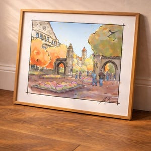 May include: Watercolor painting of a university campus scene in a wooden frame. The artwork depicts a courtyard with arched entryways, buildings, and people. Autumn foliage in shades of orange and yellow adds color to the scene.