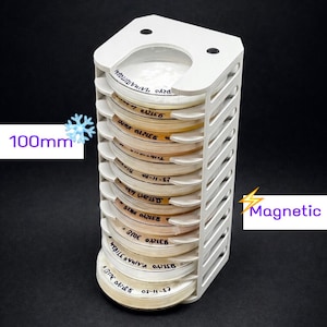 May include: A white, 3D-printed holder with multiple slots, designed to hold several round, labeled containers. The containers are stacked vertically, and the holder is approximately 100mm in height. The word "Magnetic" is displayed.