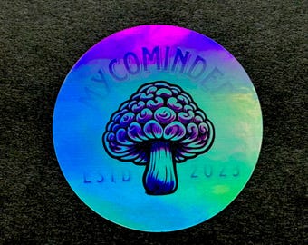 Puede incluir: Pegatina holográfica redonda con un diseño de hongo psicodélico. El texto "MYCOMINDE" está arqueado en la parte superior y "ESTD 2023" en la inferior. El hongo está detallado en azul y morado, con un efecto iridiscente.