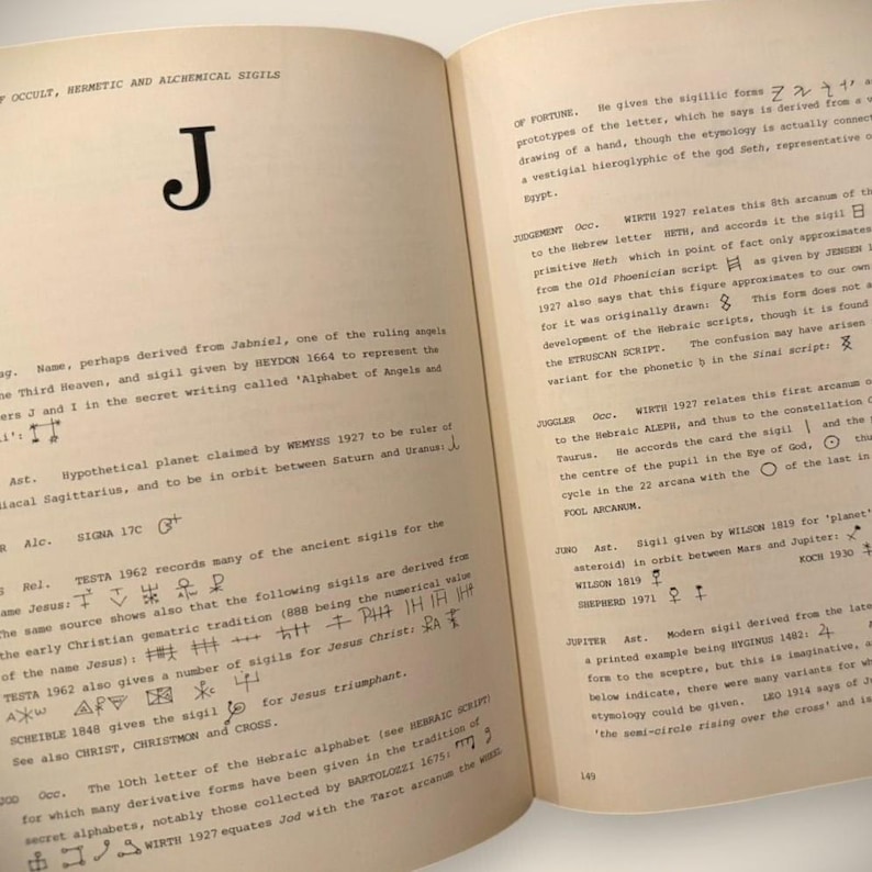 May include: Open book with text and symbols related to occultism, hermeticism, and alchemy. The left page features a large letter "J" and various symbols. The right page contains text discussing sigillic forms and the Hebrew alphabet. The pages are aged.