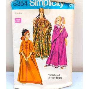 May include: Vintage Simplicity sewing pattern featuring illustrations of three different caftan designs. The pattern envelope is blue and white with the number 8354 at the top. The designs include a long orange caftan, a patterned caftan, and a pink caftan.