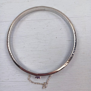 Pode incluir: Uma caneca de cerâmica branca com uma alça preta e o texto "But First, Coffee" em negrito preto. A caneca está sobre um fundo neutro, destacando seu design simples.