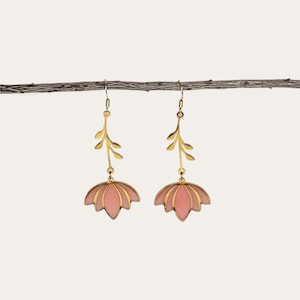 May include: A pair of gold-toned drop earrings featuring a delicate stem with three small leaves extending upward from a stylized, fan-shaped flower petal design. The petals are filled with a soft, matte pink enamel and outlined in polished gold metal.