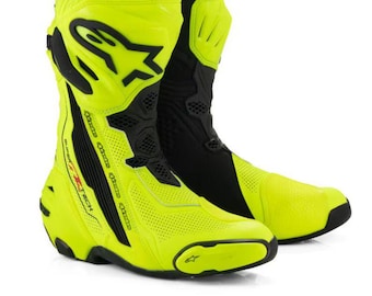 Könnte beinhalten: Ein Paar neongelbe und schwarze Motorrad-Rennstiefel mit dem Alpinestars-Logo auf dem Schienbeinschutz, perforierten Einsätzen am Fuß und dem Schriftzug Supertech an der Seite der Knöchelstützstruktur.