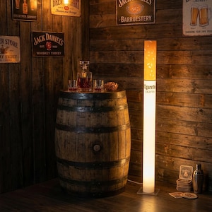 Peut inclure: Un lampadaire original en forme de cigarette, avec un design blanc et orange. Il se dresse à côté d'une table en tonneau de bois avec une carafe et des verres. Le fond présente des enseignes de bar vintage.