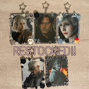 May include: Keychains featuring character portraits, framed with decorative elements like pearls, roses, and bows. The keychains have a star-shaped top and the text "RESTOCKED!!" in pink.