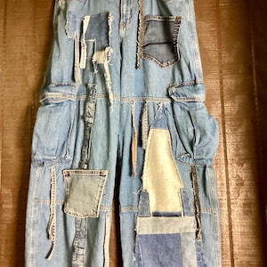 May include: Light blue denim jeans with multiple patches of varying shades of blue denim. The jeans have a high waist, cargo pockets, and a relaxed fit. The patches are sewn on, creating a unique, distressed look. The jeans are hanging on a hanger.
