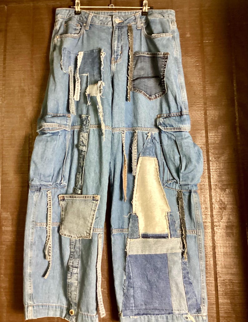 May include: Light blue denim jeans with multiple patches of varying shades of blue denim. The jeans have a high waist, cargo pockets, and a relaxed fit. The patches are sewn on, creating a unique, distressed look. The jeans are hanging on a hanger.