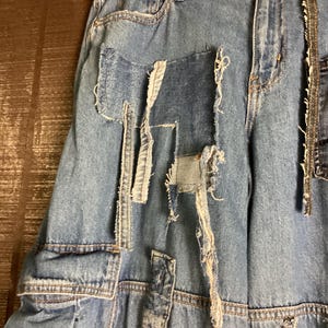 May include: Light blue denim jeans with distressed patches and frayed edges. The jeans feature a classic five-pocket design and a button and zipper closure. The patches are in various shapes and sizes, adding a unique, deconstructed look.