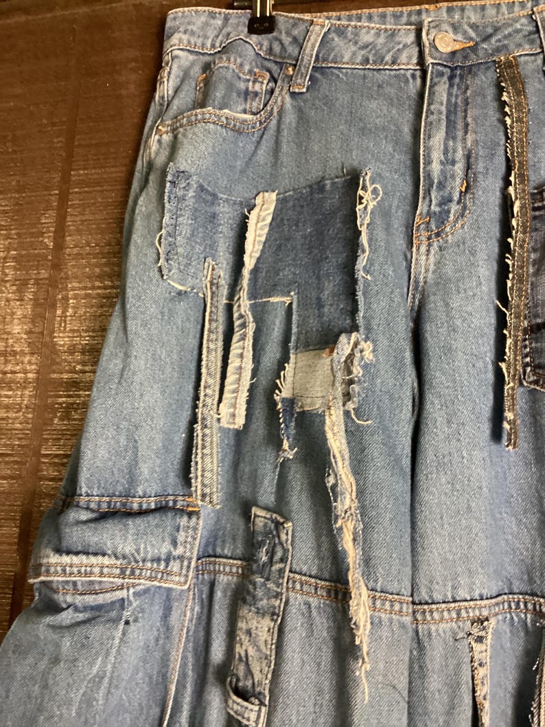 May include: Light blue denim jeans with distressed patches and frayed edges. The jeans feature a classic five-pocket design and a button and zipper closure. The patches are in various shapes and sizes, adding a unique, deconstructed look.