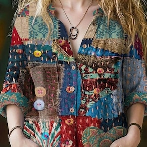 May include: A colourful patchwork shirt with a mix of patterns and shades like blue, red, and teal. The shirt features a button-down design, short sleeves, and decorative buttons. A necklace with two interlocking circles is visible.