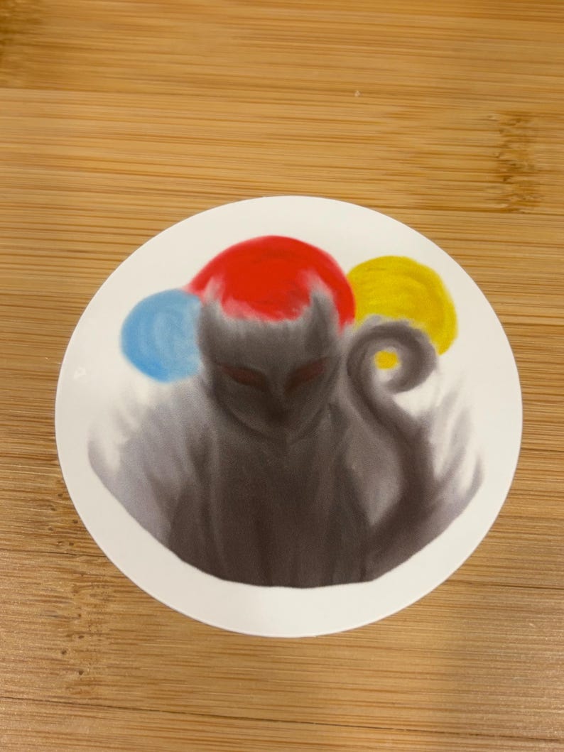 May include: A round sticker featuring a stylized, shadowy figure with a red head covering and a curled tail. The design includes blue and yellow orbs, creating a whimsical and artistic aesthetic. The sticker is on a wooden surface.