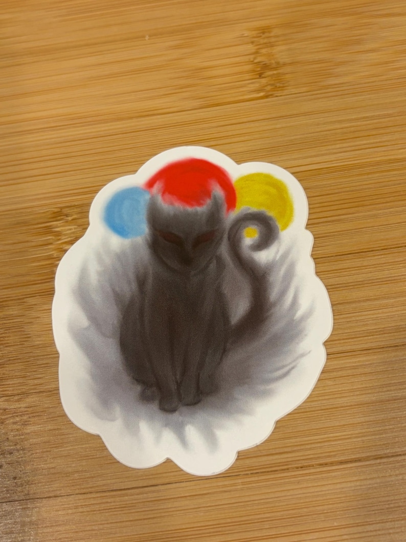 May include: A sticker featuring a stylized black cat with a red hat and three colorful orbs. The cat is sitting, with its tail curled. The sticker has a white, cloud-like border and is on a wooden surface.