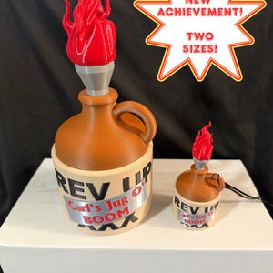 May include: Two brown and cream-colored jugs with handles, each topped with a red flame attachment. The jugs feature the text "REV UP" and "Carl's Jug O' BOOM" on the front. A star-shaped graphic above reads "NEW ACHIEVEMENT! TWO SIZES!"