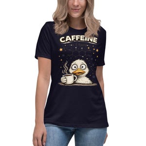 Peut inclure: T-shirt bleu marine avec le mot "CAFFEINE" au-dessus d'un canard de dessin animé tenant une tasse de café. Le canard a de grands yeux et de la vapeur s'échappe de la tasse. Le motif comprend des étoiles et des structures moléculaires.