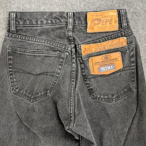Puede incluir: Primer plano de la parte trasera de unos vaqueros negros descoloridos. Los vaqueros tienen dos bolsillos traseros y un parche de cuero marrón con la marca "PEPE" y "PEPE JEANS LONDON". Los vaqueros son vintage.