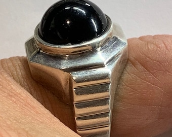 May include: A silver ring with a black gemstone set in a raised bezel. The band is textured with a series of ridges.