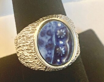 May include: A silver ring with a blue and white cameo set in a textured oval bezel.