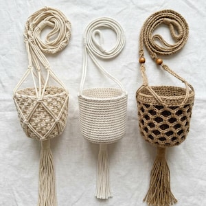 May include: Three handmade macrame plant hangers in natural tones. The hangers feature woven baskets with tassels and long cords for hanging. The designs include diamond, solid, and open weave patterns, perfect for displaying small plants.