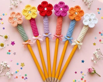 Puede incluir: Seis lápices amarillos, cada uno coronado con una flor de ganchillo de diferentes colores: melocotón, amarillo, rojo, rosa, naranja y blanco. Cada flor tiene un centro de pedrería. Los lápices tienen mangas de ganchillo a juego y pequeños lazos.