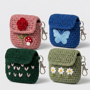 May include: Four square crochet cases for wireless earbuds, each featuring a metal lobster clasp. The pink case has a red rose and mushroom, the blue case has a light blue butterfly, the dark green case has pink hearts, and the sage green case has white daisies.