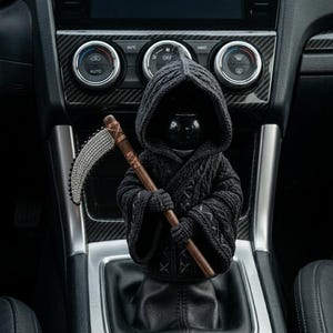 May include: A black crocheted Grim Reaper car accessory, complete with a hooded cloak and a scythe. The figure is positioned on a car's gear shift, adding a unique, gothic touch to the vehicle's interior. The scythe is approximately 6 inches long.
