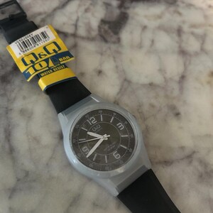 Puede incluir: Un reloj de pulsera de cuarzo Q&Q con correa de silicona negra y caja gris claro. La esfera negra presenta n&uacute;meros ar&aacute;bigos blancos en las posiciones 12, 3, 6 y 9, con manecillas blancas. Una etiqueta amarilla y azul indica 10 BAR.