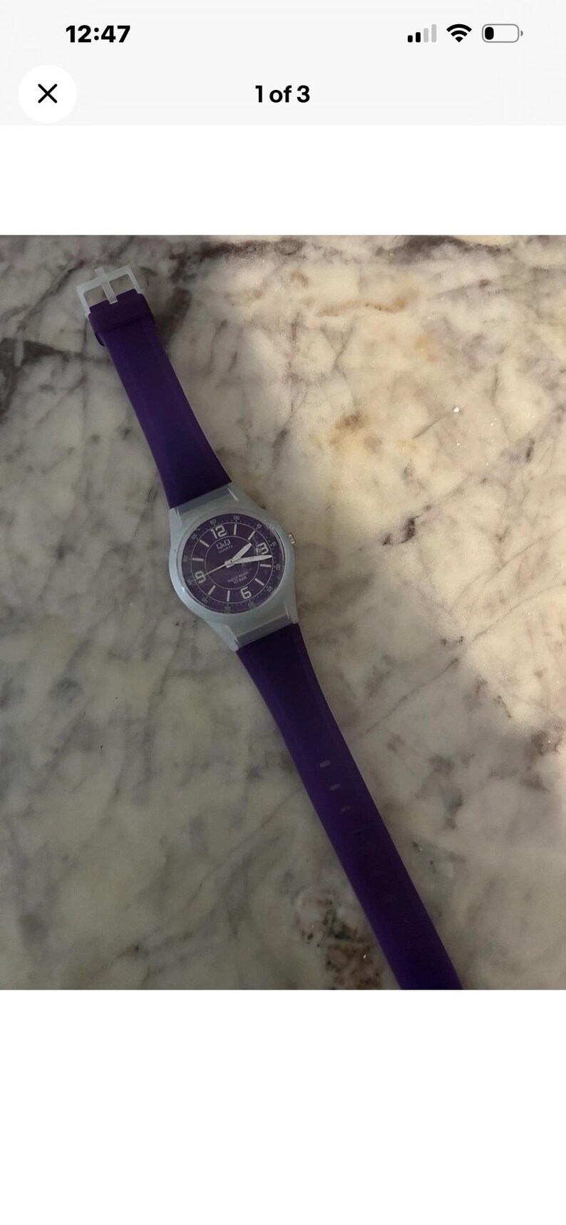 Puede incluir: Un reloj de pulsera de cuarzo Q&Q con una correa de silicona de color morado vibrante y una esfera circular morada a juego. El reloj tiene una caja de pl&aacute;stico gris claro, marcadores de hora blancos y manecillas blancas. La esfera muestra el 12 y el 6.