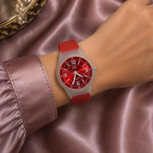 Op de afbeelding: Een Q&Q quartz horloge met een levendige rode sunray wijzerplaat met witte Arabische cijfers op de 12, 3, 6 en 9 uur posities, zilverkleurige wijzers, een doorschijnende witte hars behuizing en een flexibele rode siliconen horlogeband.
