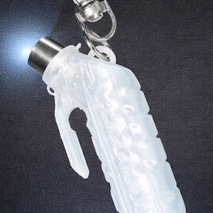 May include: A clear, plastic grenade-shaped keychain flashlight with a silver metal clip. The flashlight emits a bright blue light from the top. The keychain is on a dark background.