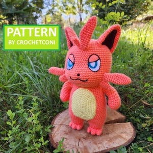 May include: A handmade crochet doll in shades of orange, with a yellow belly and blue eyes. The doll has small wings and is standing on a wooden surface. The text "PATTERN BY CROCHETCONI" is in a green box.