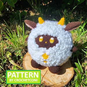 May include: A handmade crochet sheep plushie with a fluffy white body, brown face, ears, and feet, and yellow horns. The plushie is sitting on a wooden slice. The image includes the text "PATTERN BY CROCHETCONI".