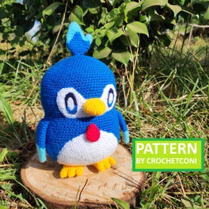 May include: A handmade blue, white, yellow, and red crochet penguin doll. The penguin has large oval eyes, a yellow beak, and yellow feet. The doll is sitting on a wooden slice. The image includes the text "PATTERN BY CROCHETCONI".