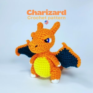Puede incluir: Figura de Charizard de ganchillo naranja, con alas azules y vientre amarillo. El texto "Charizard Crochet pattern" está arriba. Tiene detalles blancos y un ojo azul. Hecho a mano.
