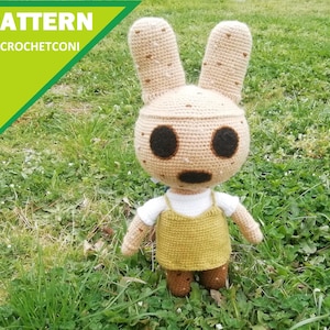 Puede incluir: Una muñeca de conejito de ganchillo con ojos grandes y oscuros y una boca cosida. La muñeca lleva un vestido de peto amarillo sobre una camisa blanca. El texto "PATTERN BY CROCHETCONI" está en la esquina superior izquierda.